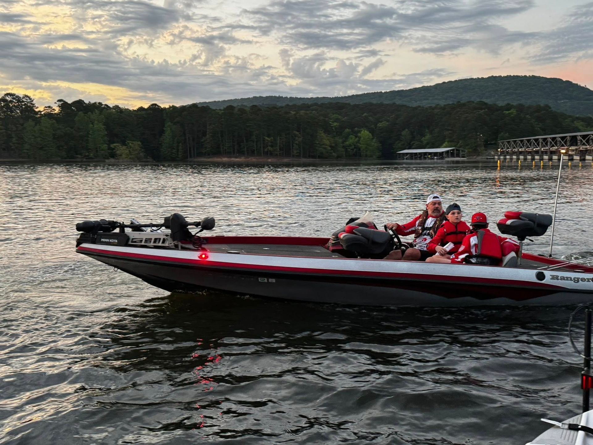Red fishing boat with anglers on a lake at sunset, wooded shoreline in the background