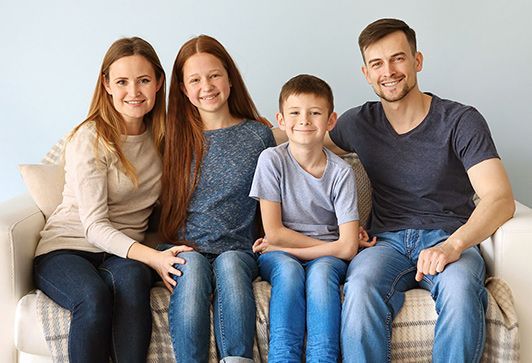 Family of four smiling on a couch in a bright room.