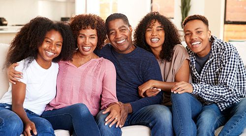 Family of five smiling, sitting together on a couch, indoors.