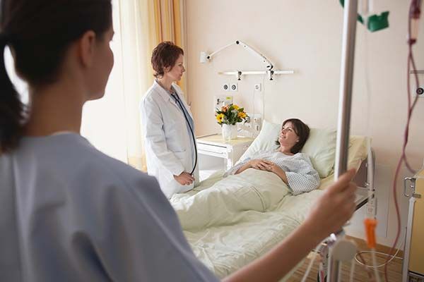 Nurse holding IV bag, doctor talks to patient in hospital bed.