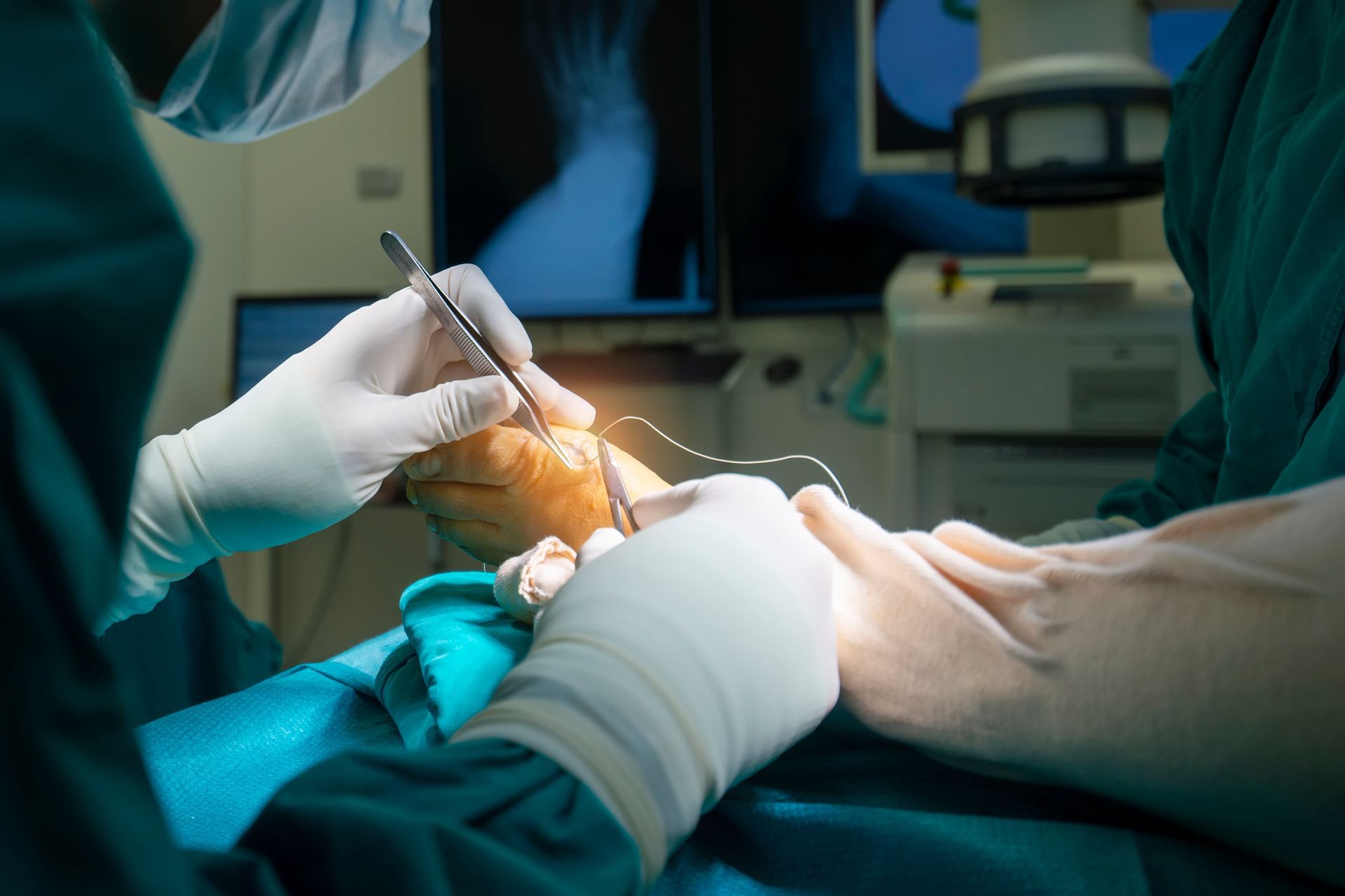 Surgeons in green scrubs operating on a foot under bright lights. X-ray visible in background.