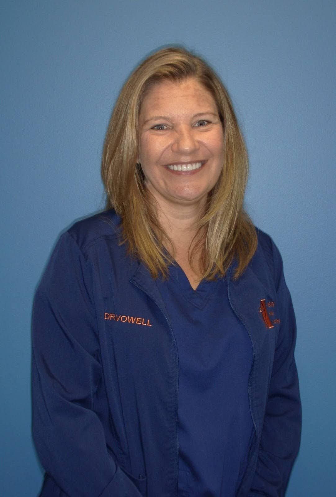 Woman in blue scrubs smiles at the camera against a blue background.