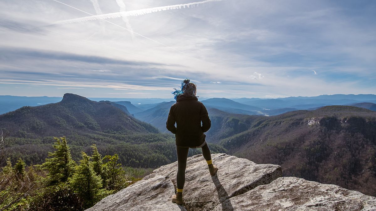A woman stands on a cliff overlooking mountains.
