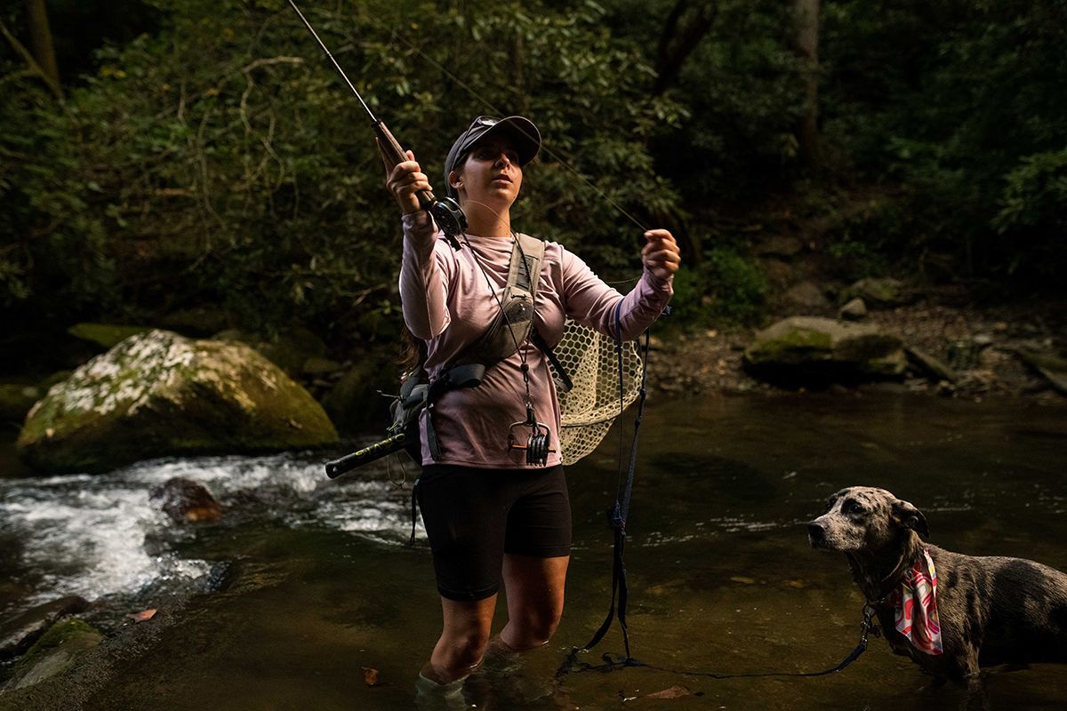 A woman is fishing in a river with her dog.