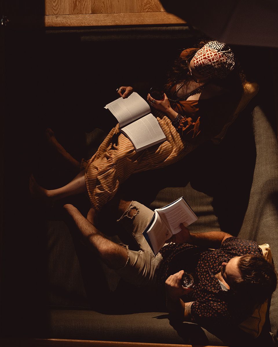 Two people seated, reading books, lit by sunlight.