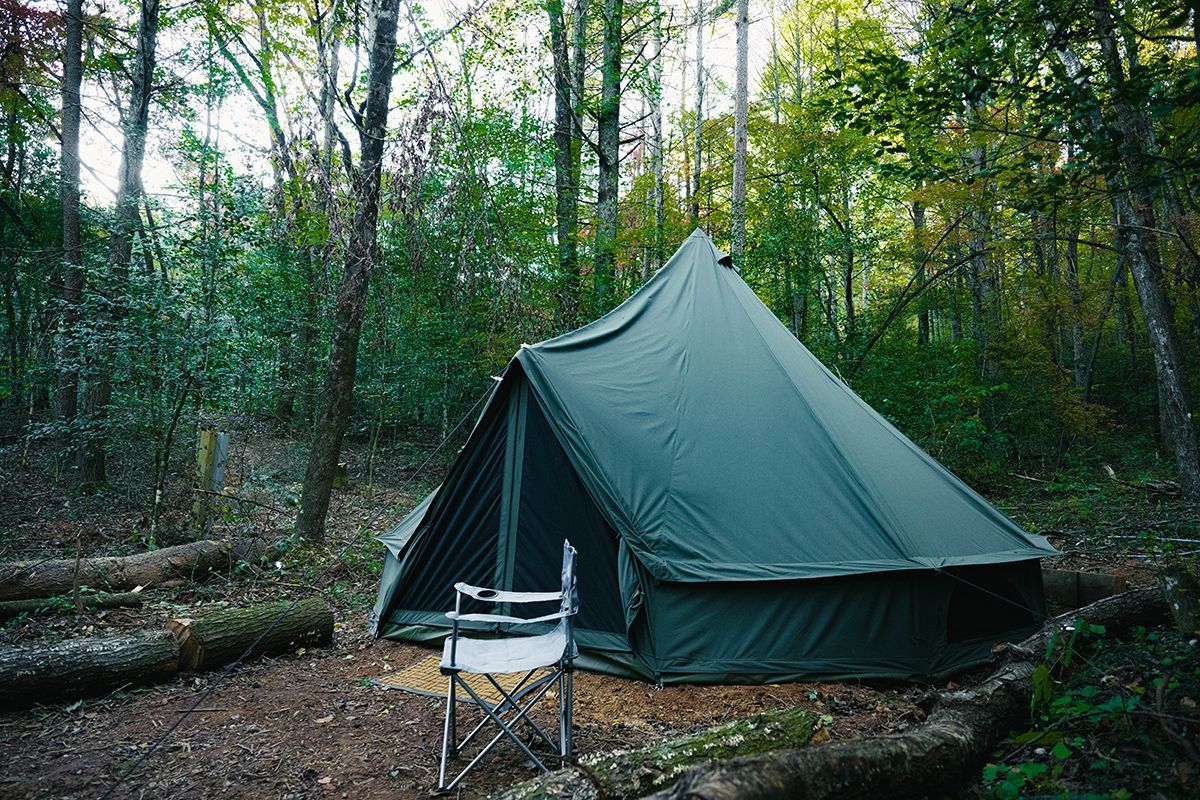 Green tent set up in a forest, with a folding chair.