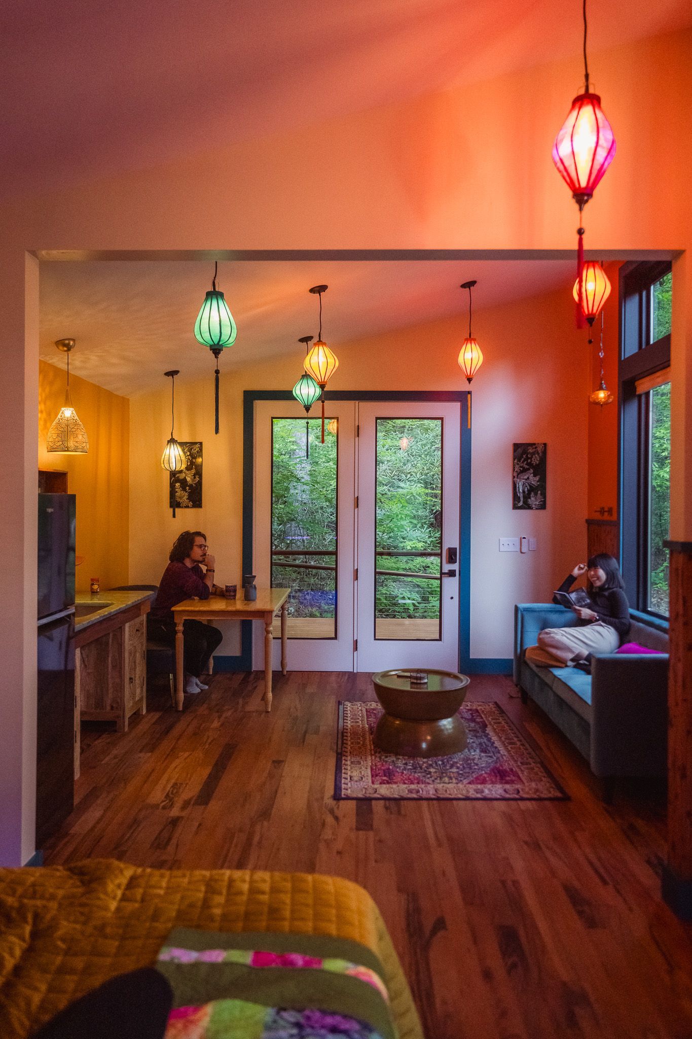 Interior of a tiny house with loft.  Wooden ladder, orange walls, kitchen in the left. Bathroom door visible.