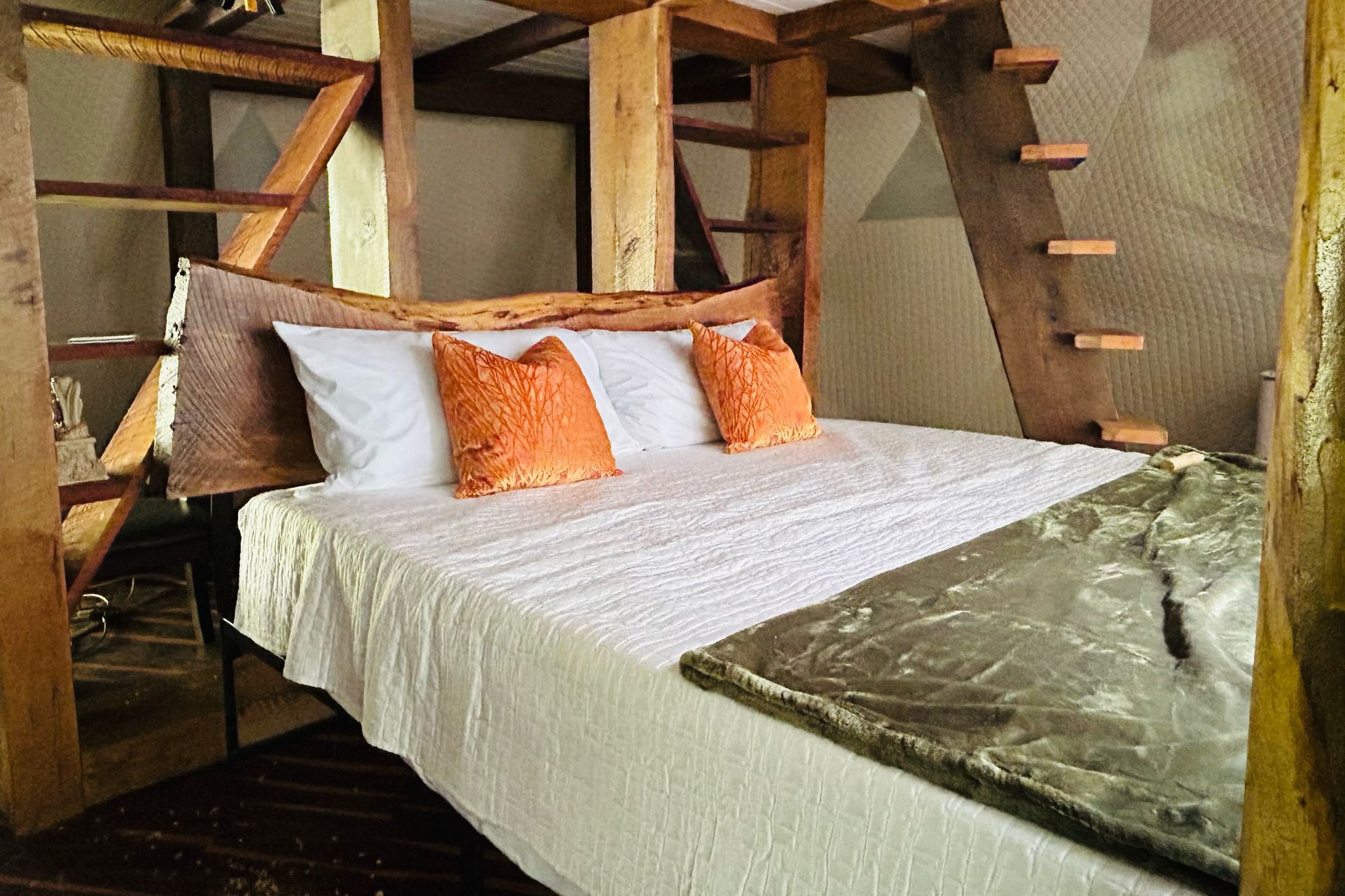 Bedroom with a wooden frame bed, white bedding, and orange pillows. A wooden ladder leads to a loft.