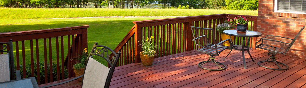 Wooden deck with chairs, table, and potted plants overlooking a green lawn.