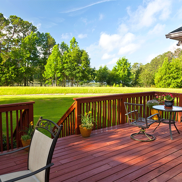 Wooden deck with outdoor seating overlooking a green lawn and trees under a blue sky.