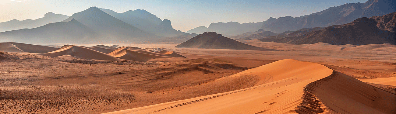 Sandy desert landscape with rolling dunes, distant mountains, and a hazy sky.