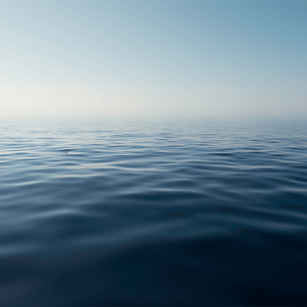 Calm, dark blue ocean meets a hazy, pale blue sky at the horizon.
