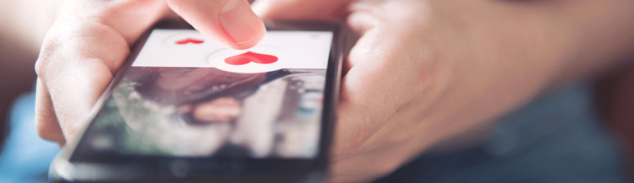 Close-up of hands using a smartphone to interact with a photo overlaid with red heart icons.