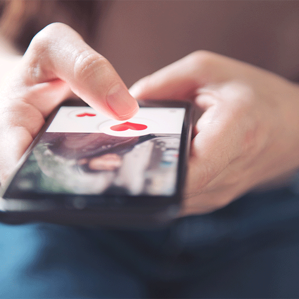 Close-up of hands using a smartphone to interact with a dating app profile displaying a heart icon.