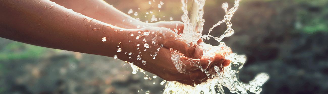 Hands cupped, water streams down and splashes, set against a blurred green background.