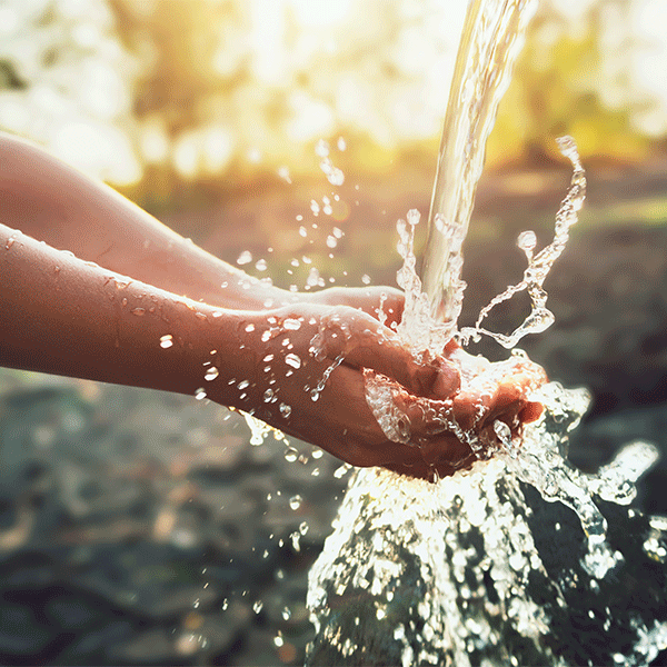 Water pouring into cupped hands outdoors, splashing in sunlight.
