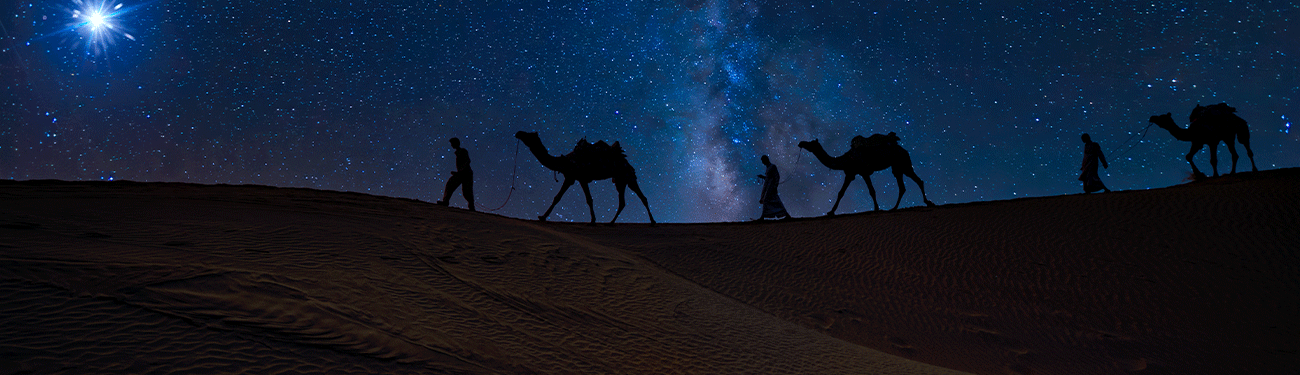 Silhouetted figures on camels trek across a desert under a starry night sky, with a bright star overhead.
