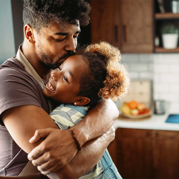 Man hugging and kissing child in a kitchen; both smiling.
