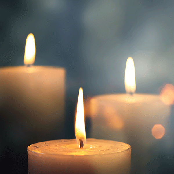 Three lit white candles with soft, warm flames against a blurred blue background.