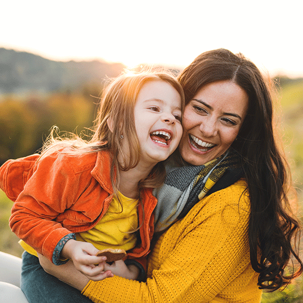 Woman and child laughing outdoors, embracing in a sunny field.
