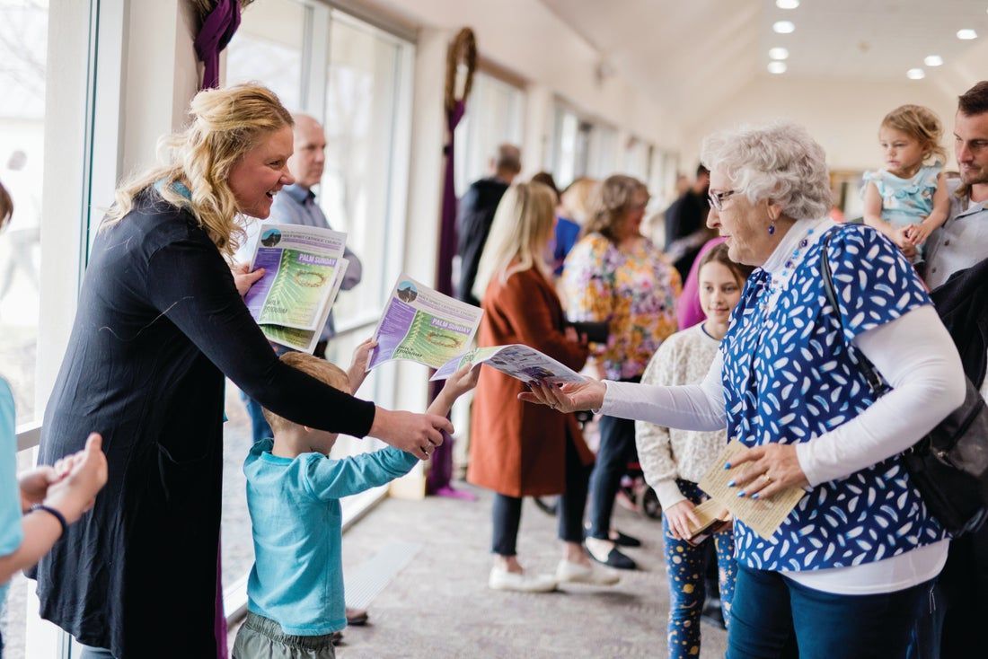 A child is hanid a bulletin to a woman in a crowded entry way.