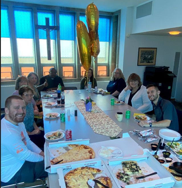 A group of people are sitting around a with food smiling at the camera.
