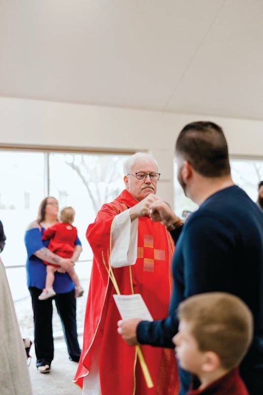 A priest is fist pumping a man with a woman holding a baby in the background.
