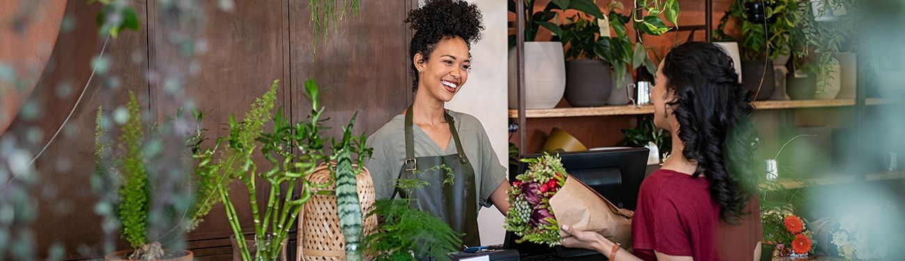 A florist hands a woman some flowers in a shop filled with plants.
