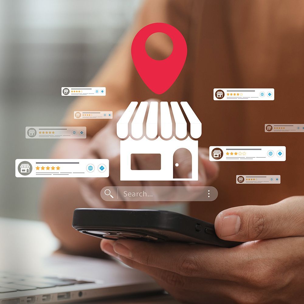 Hand holding smartphone with a red map pin above a storefront icon and review ratings, suggesting local business search