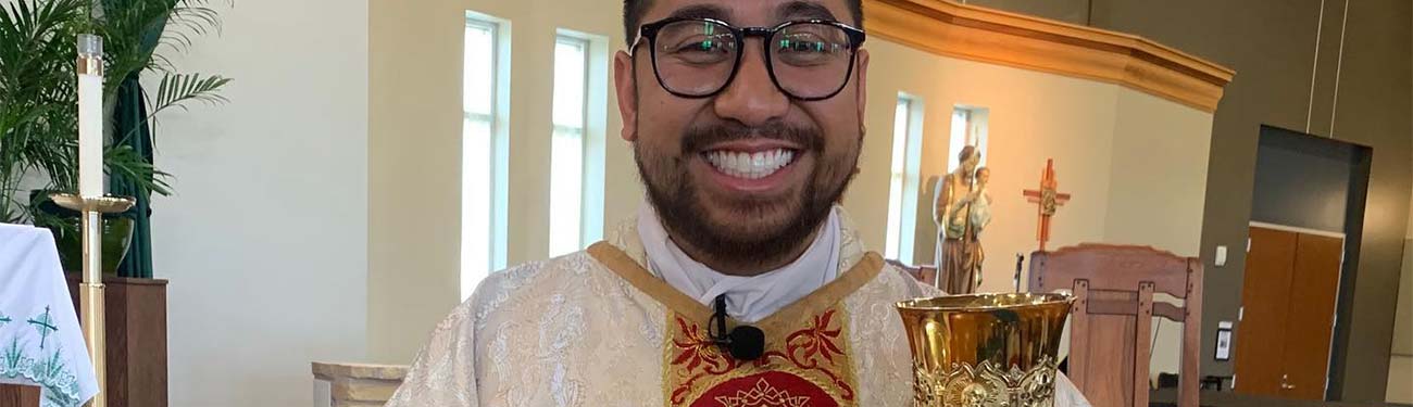 A Priest with glasses is holding a chalice in a church.