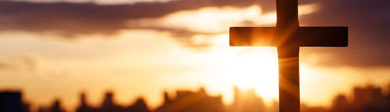 Silhouette of a cross at sunset with warm orange sky and blurred background.