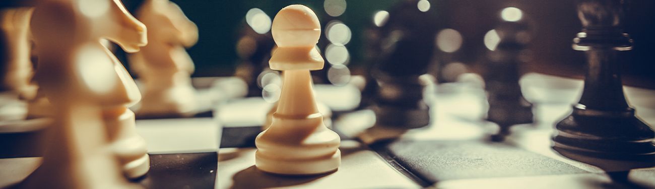 Chess pieces on a board, with a white queen in focus and blurred pieces in the background.