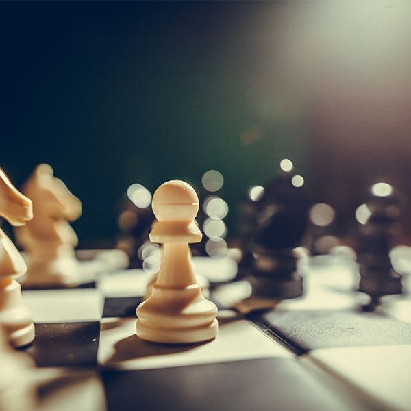 Close-up of chess pieces on a board, with a white pawn in focus and blurred pieces in the background