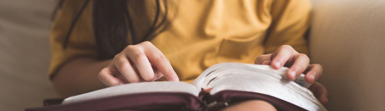 Hands turning the pages of an open book on a table under warm light.