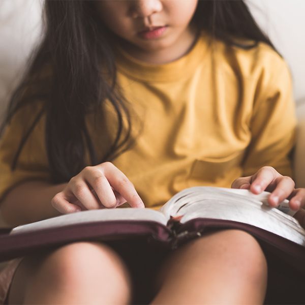 Child reading a book in a cozy indoor setting, hands on open pages.