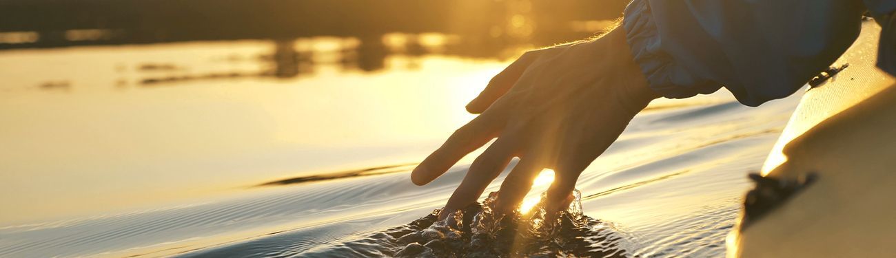 Hand gliding over a sunlit surfboard at sunset, with golden water in the background.