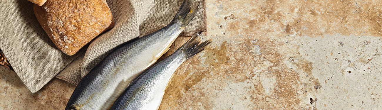 Two fresh fish beside a loaf of bread on a rustic stone surface
