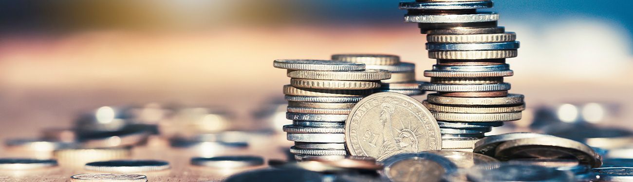 Piles of coins, some stacked, in a close-up view with a blurry background, suggesting wealth or savings.
