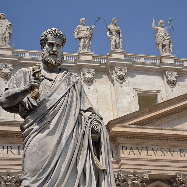 Statue of Saint Peter before St. Peter’s Basilica, with marble apostles on the roof against a blue sky