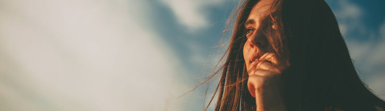 Close-up of a long-haired person gazing upward against a bright, cloudy sky.