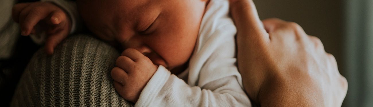 Close-up of a sleeping baby nestled on someone's shoulder. A hand supports the child.