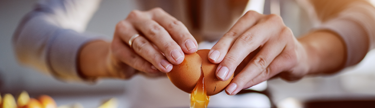 Hands cracking an egg into a bowl on a kitchen counter.