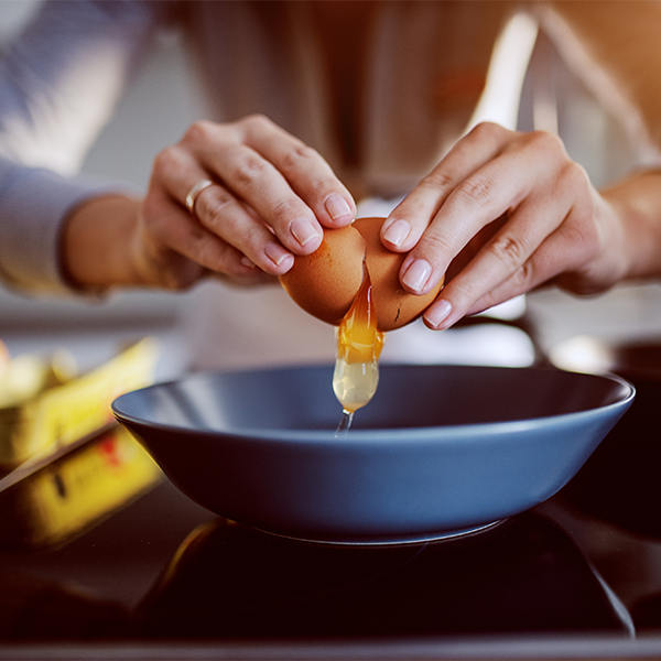 Hands cracking an egg into a black bowl in a kitchen.