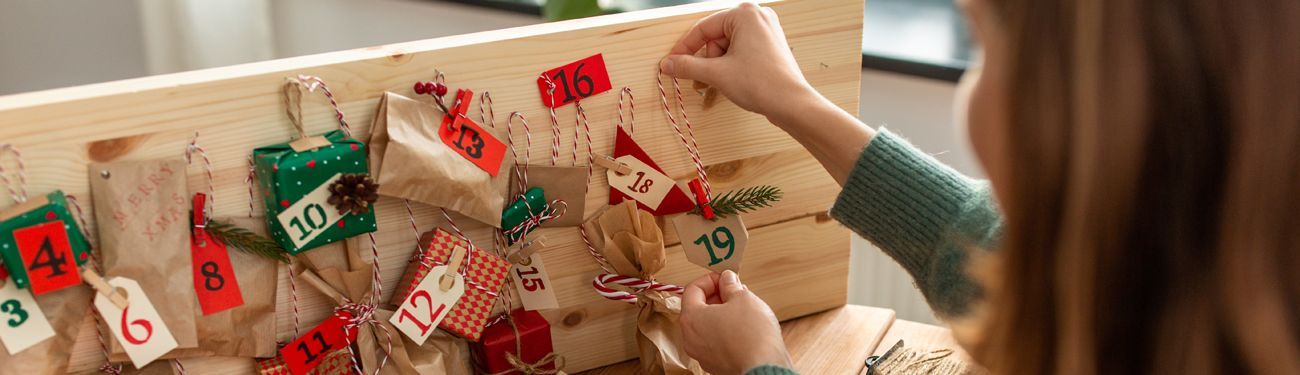 A woman is putting decorations on a wooden advent calendar.