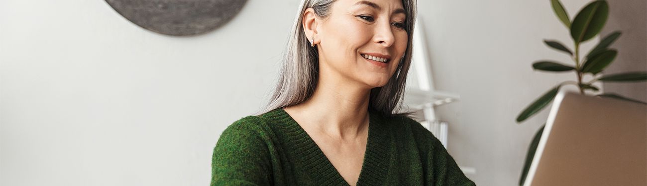 A woman in a green sweater is sitting in front of a laptop computer.