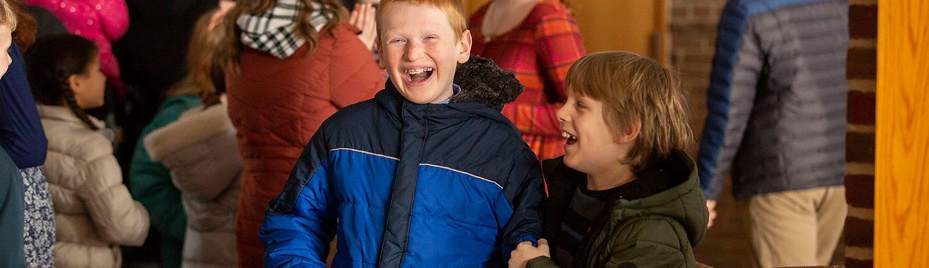 Two kids laughing together with more kids hanging out in the background.