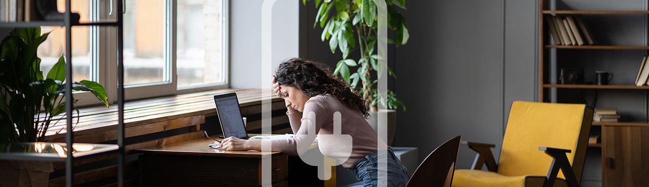 A woman is sitting at a desk in front of a laptop computer with her head resting on her hand.