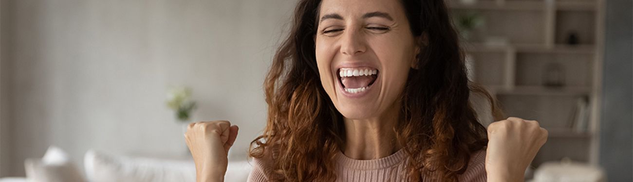 An excited woman is sitting on a couch with her arms in the air.