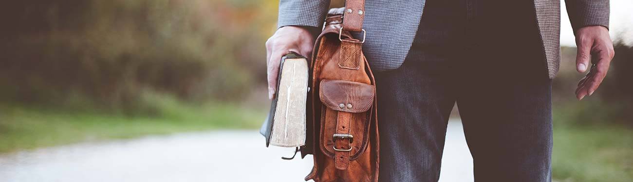 A man is walking down a road holding a book and a briefcase.