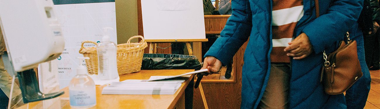 A woman in a blue coat is standing in front of a table grabbing a bulletin.